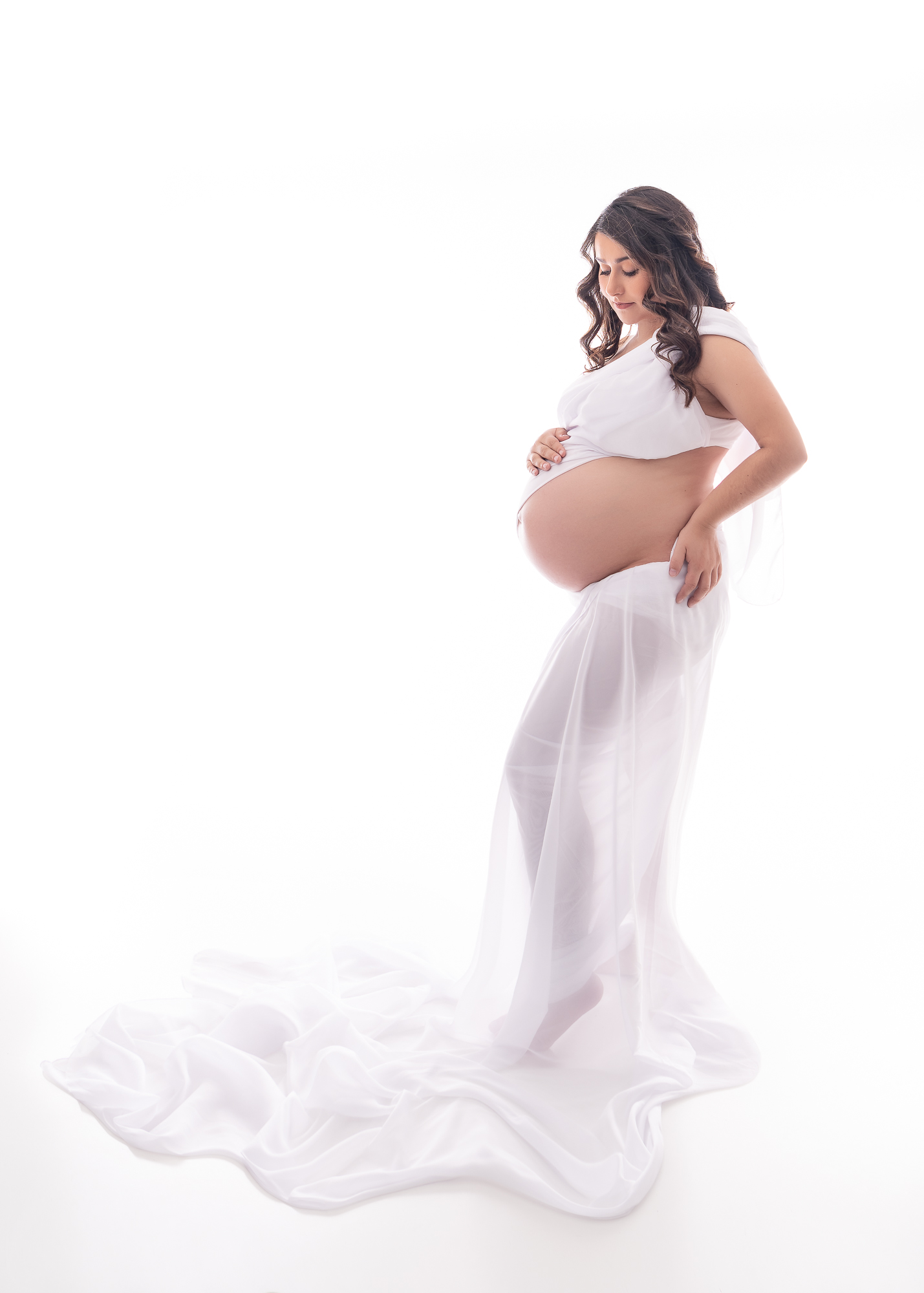 pregnant woman dressed in white top and sheer skirt, holding her belly Bend Birth Center
