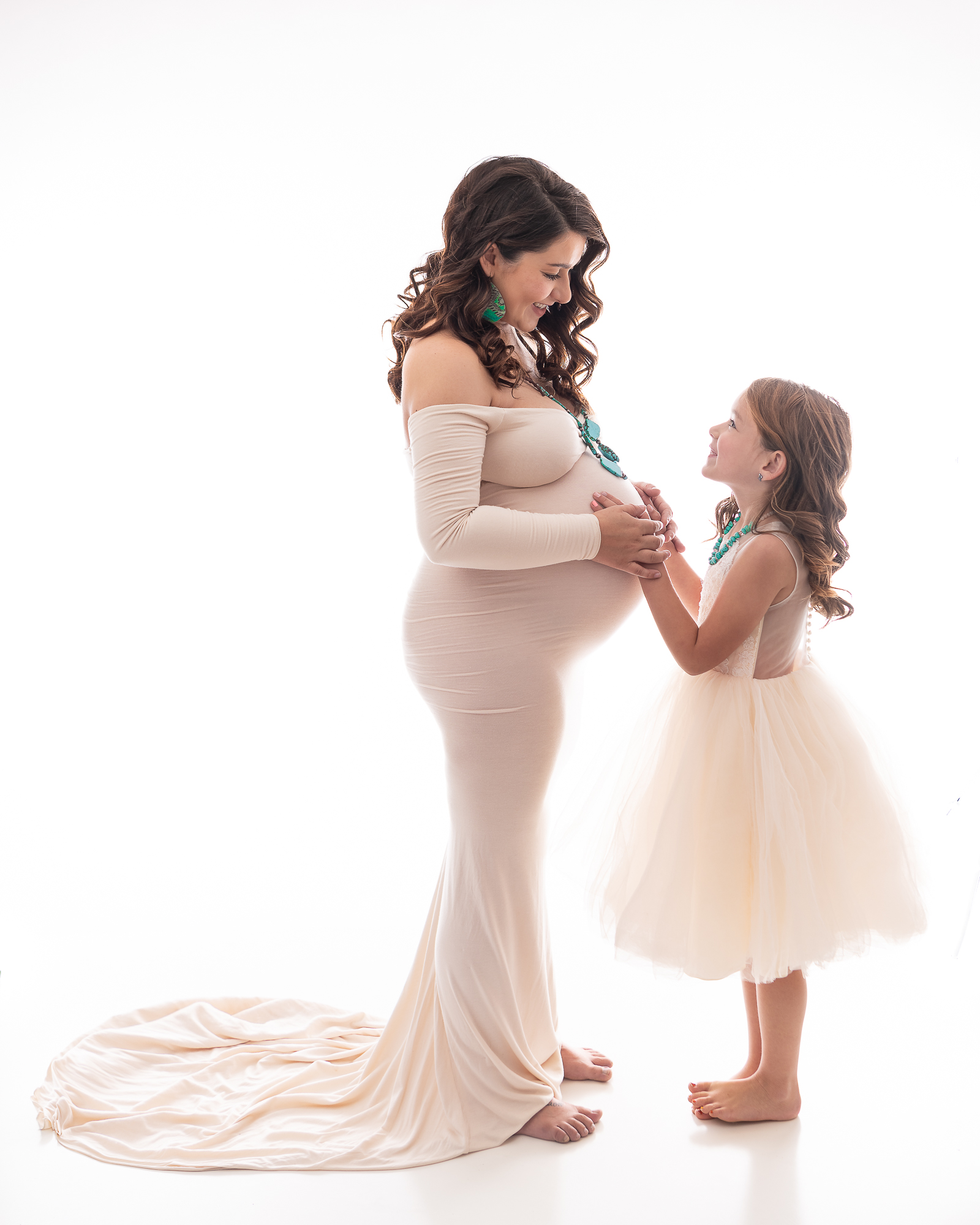 Mom to be in white gown with daughter holding her belly