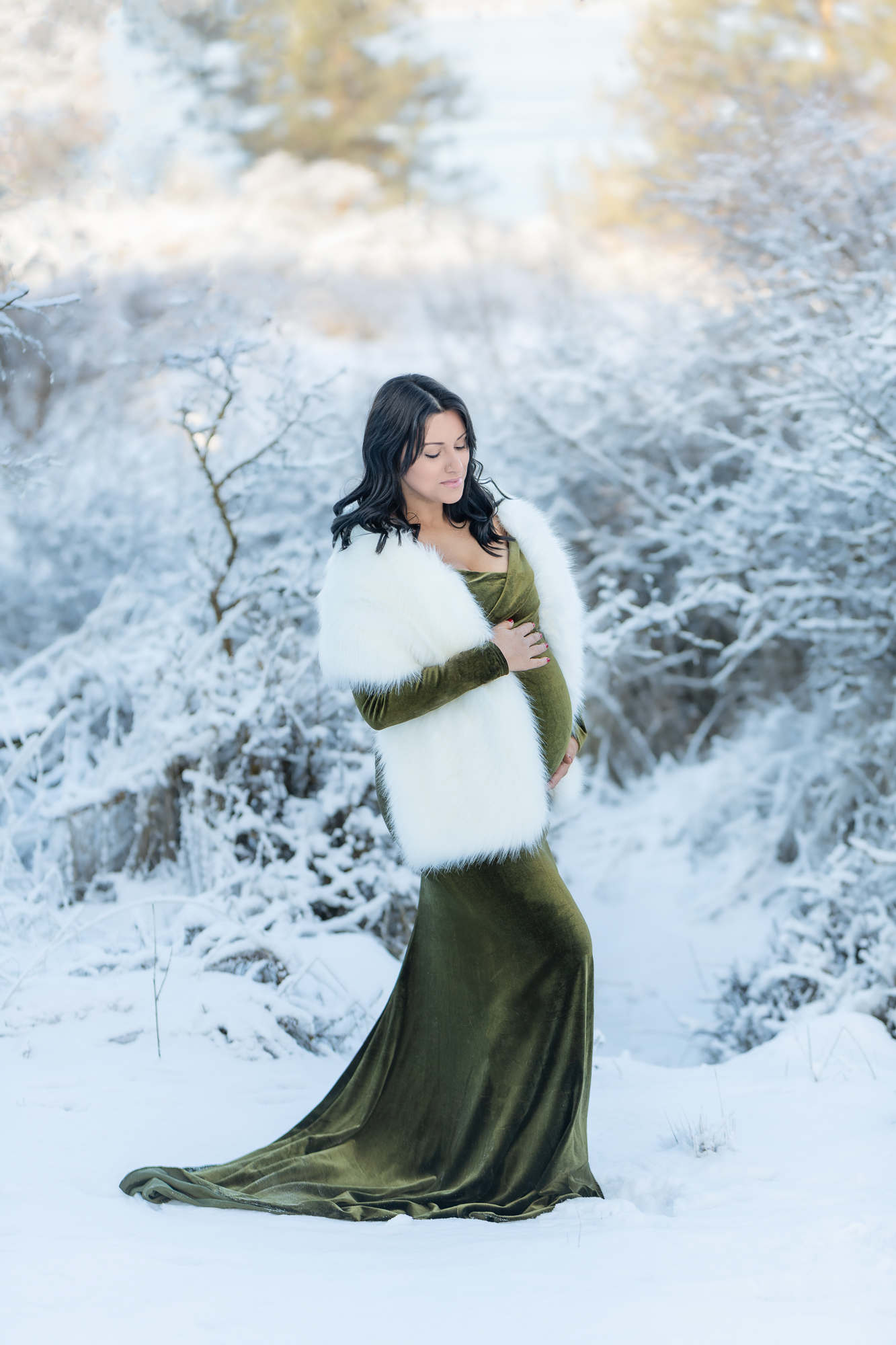 pregnant woman in green dress and white fur standing in the snow