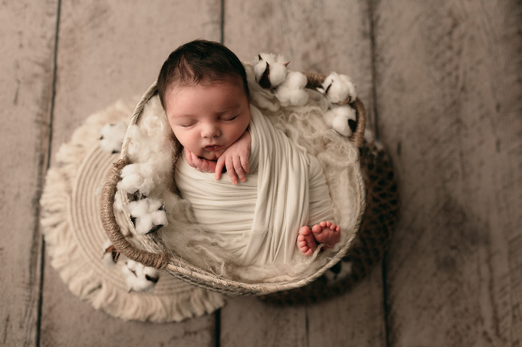 newborn baby wrapped in neutral colors with cotton in a basket