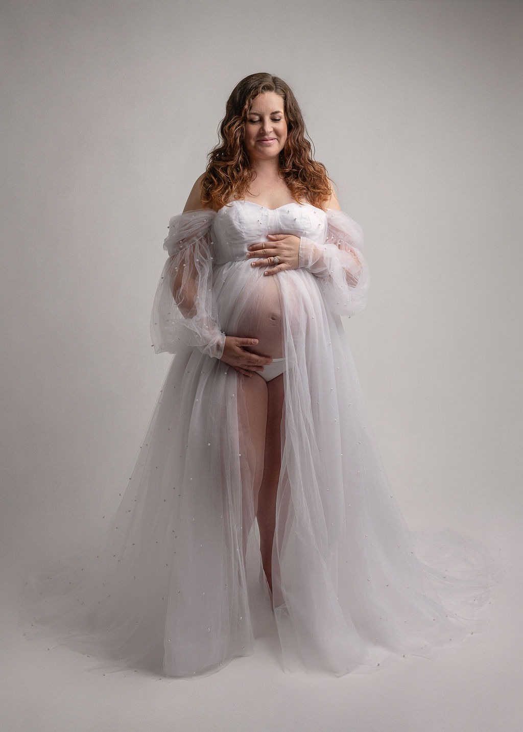 mom to be in a grey tulle maternity gown holding her belly Be Well Massage Medford
