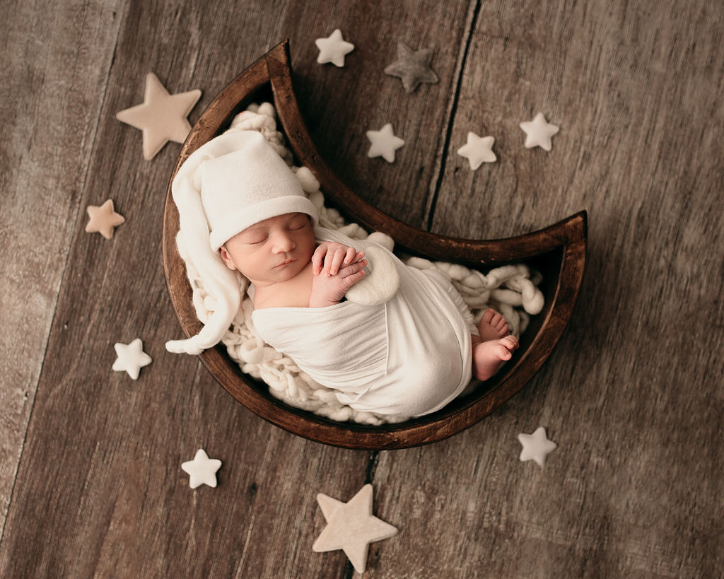 newborn baby wrapped in white with a hat laying bundled in a moon basket with stars surrounding them My Little Peanut Medford