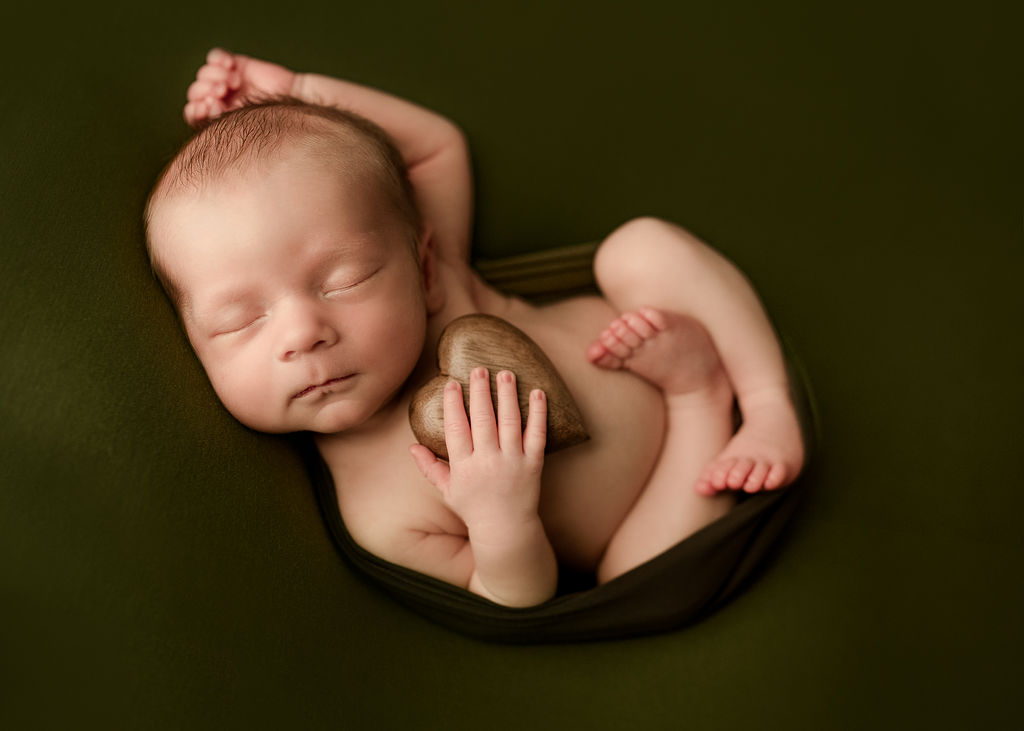 newborn baby wrapped in forest green holding a gold heart against their chest Southern Oregon Pediatrics