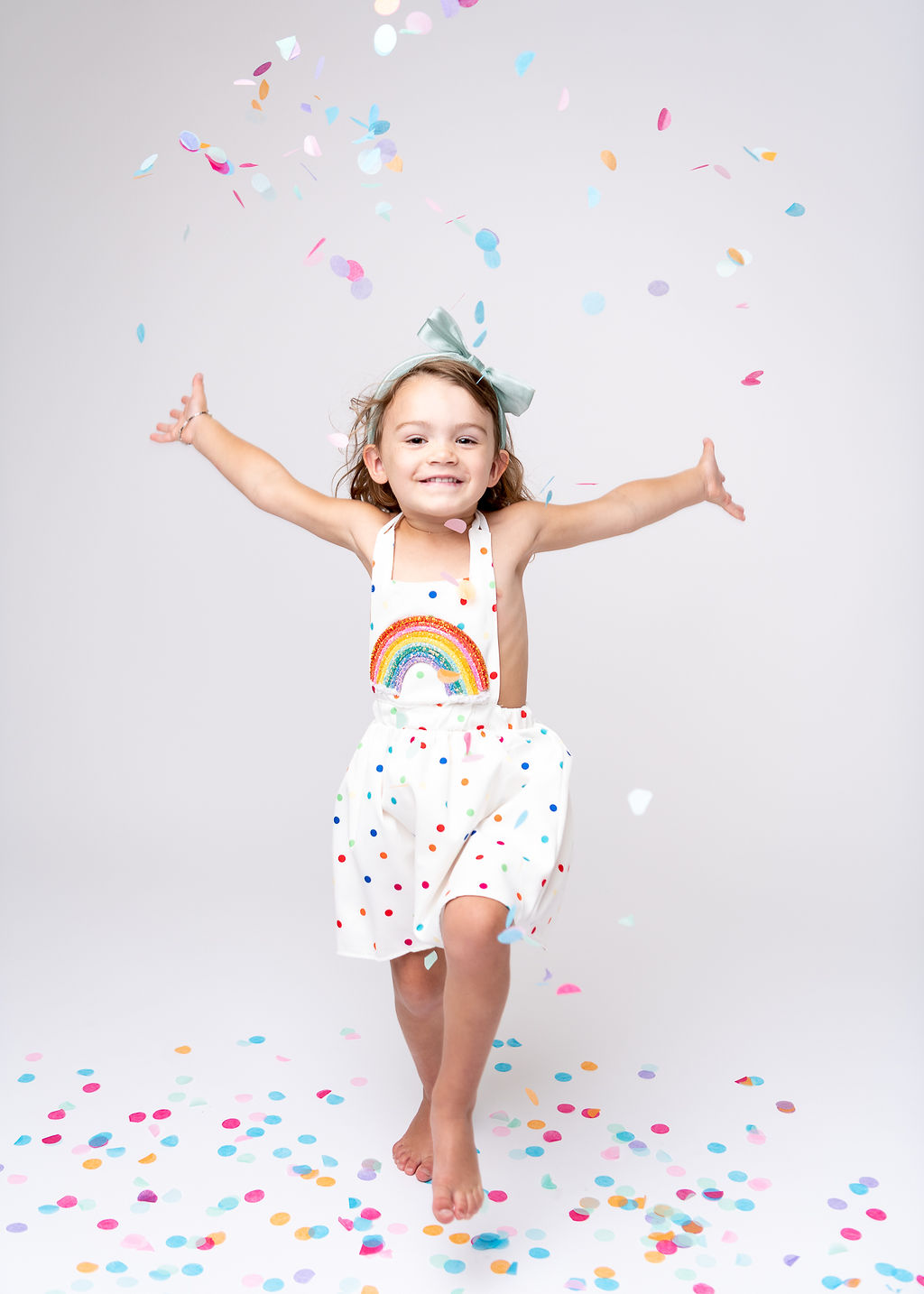 Little girl in rainbow dress throwing confetti in the air Southern Oregon Pediatrics