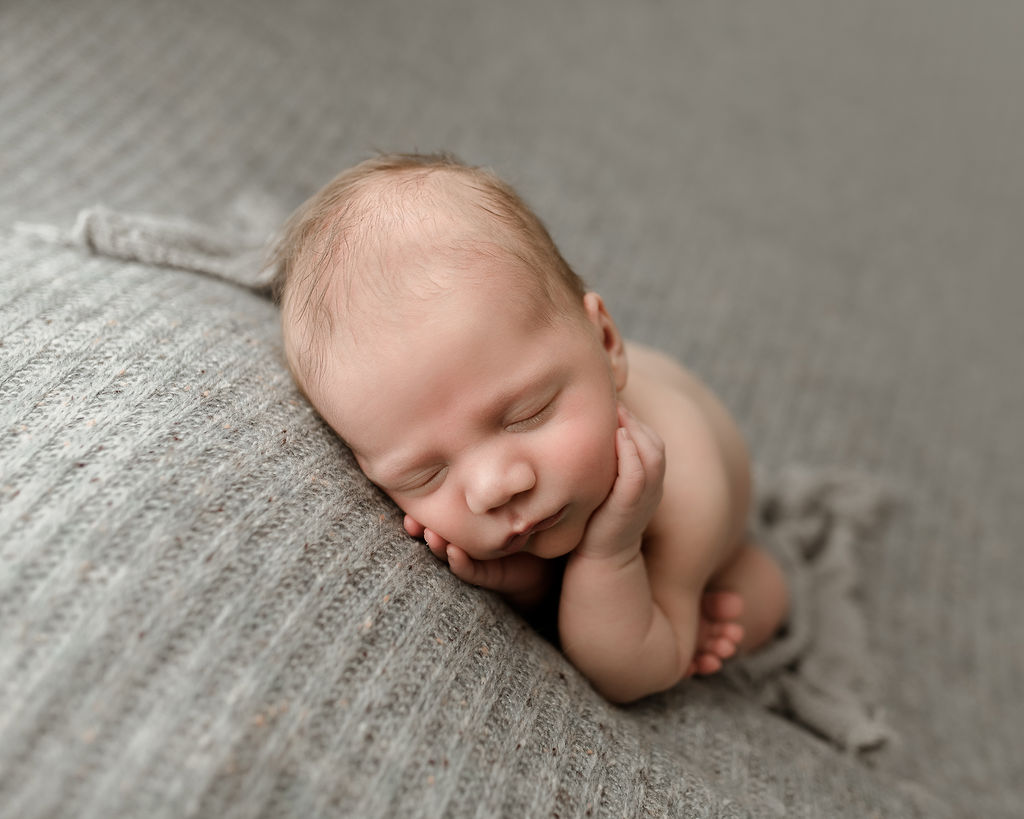 newborn baby wrapped in grey and laying on a grey blanket
