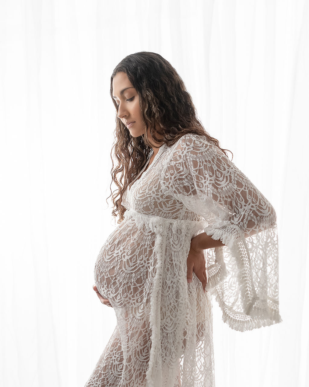 mom to be in lace white maternity gown holding her bump and looking down Ashland Yoga Center
