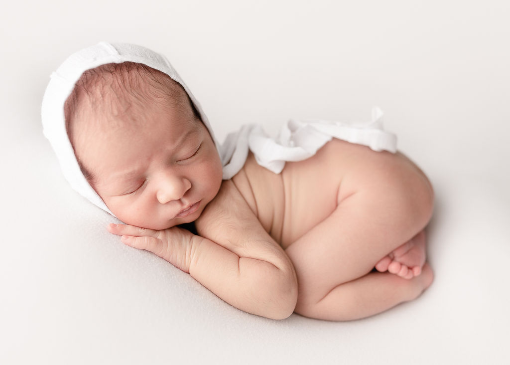newborn baby in white bonnet sleeping on it's hands