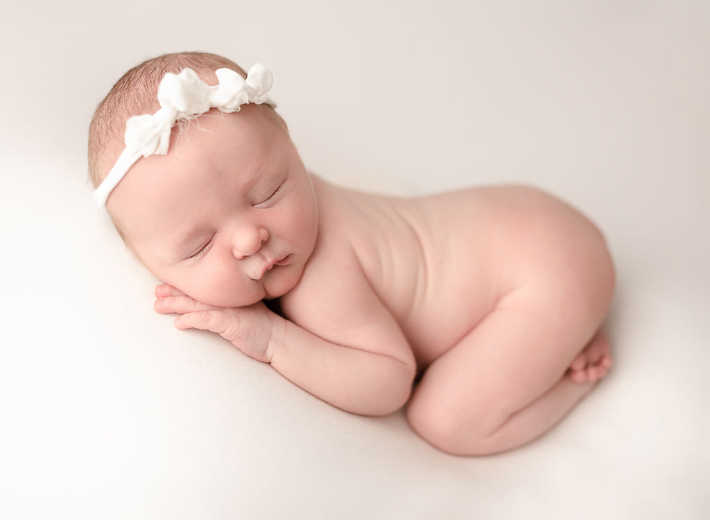 newborn baby girl wearing a white headband sleeping on her stomach