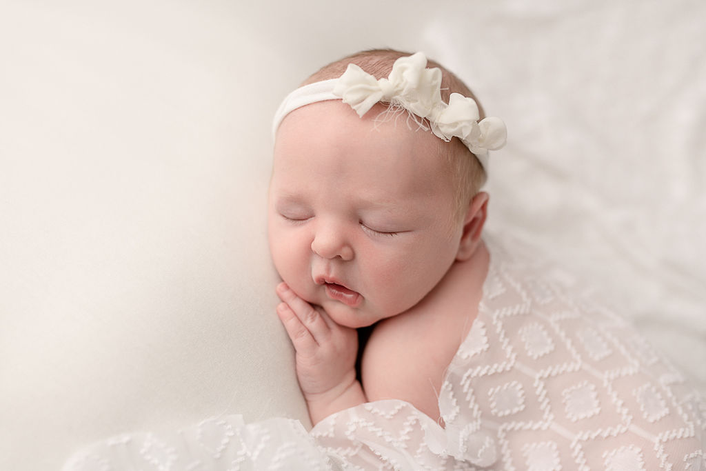 newborn baby girl wearing a white flower headband and covered in a sheer white blanket Medford Pediatricians