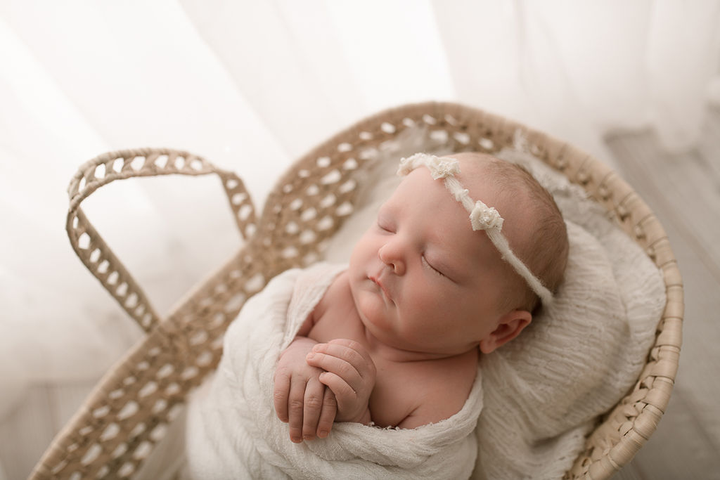 newborn baby girl in a white wrap laying peacefully in a basket