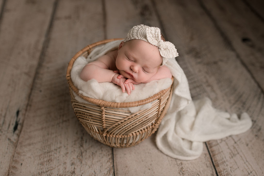 newborn baby with white bow in her hair sleeping in a basket on her hands Medford Pediatricians