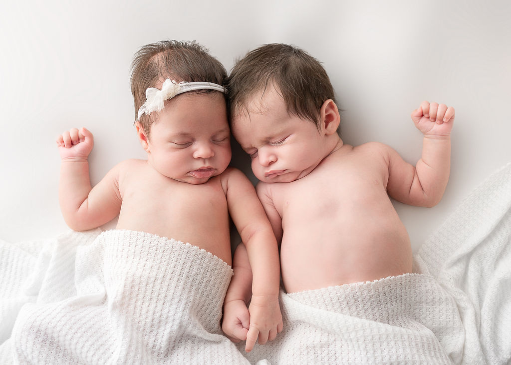 newborn twins holding hands with a white cloth over them Central Oregon Pediatric Associates