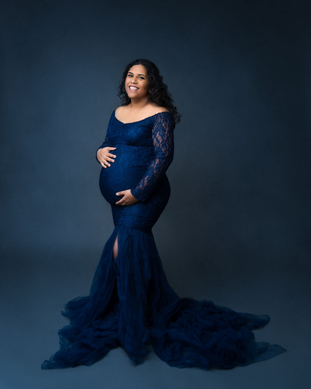 mom to be in dark blue maternity gown cradling her bump