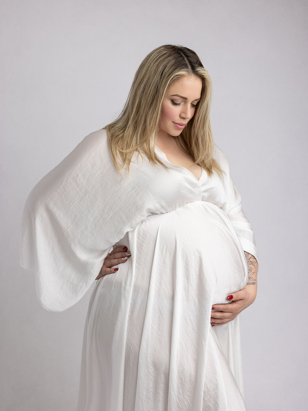 pregnant woman in white flowing maternity gown holding and looking down at her bump St. Charles Birthing Center