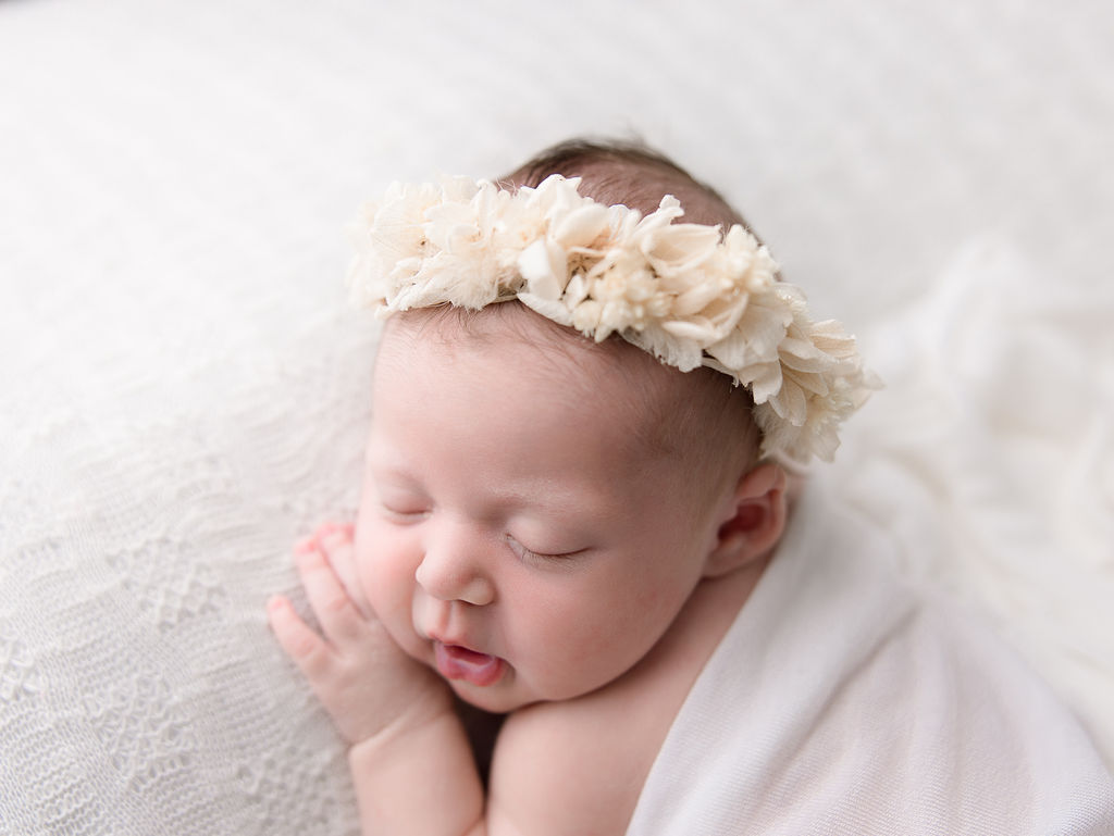 newborn baby in white with a flower crown sleeping on her stomach